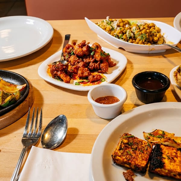A table laden with various Indian dishes, including paneer, samosas, and chickpea salad.