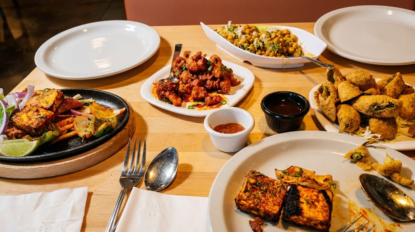 A table laden with various Indian dishes, including paneer, samosas, and chickpea salad.