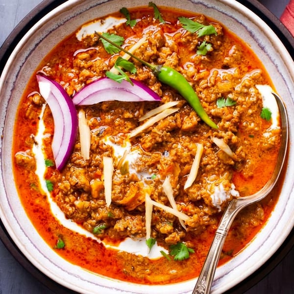 Keema curry with red onions, green chili, ginger, and naan bread on a dark table.