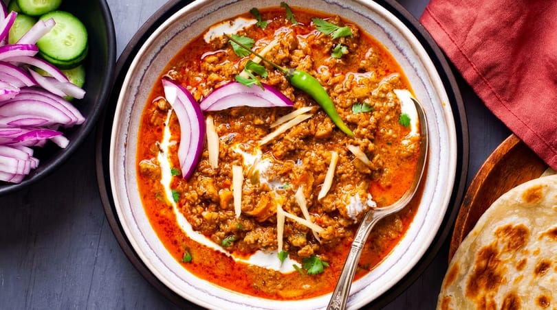 Keema curry with red onions, green chili, ginger, and naan bread on a dark table.