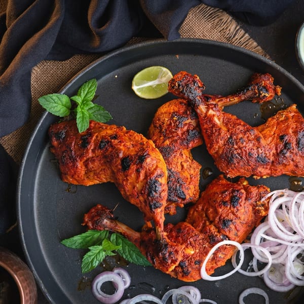 Tandoori chicken drumsticks and thighs on a black plate with mint, lime, and onion rings.