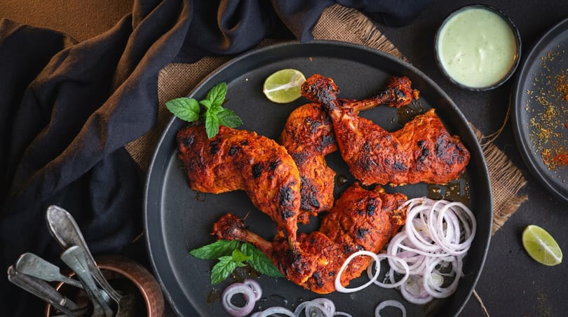 Tandoori chicken drumsticks and thighs on a black plate with mint, lime, and onion rings.