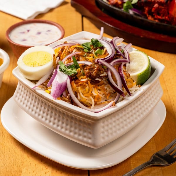 Biryani with egg, red onions, and lime, served with sauces and a soda on a wooden table.